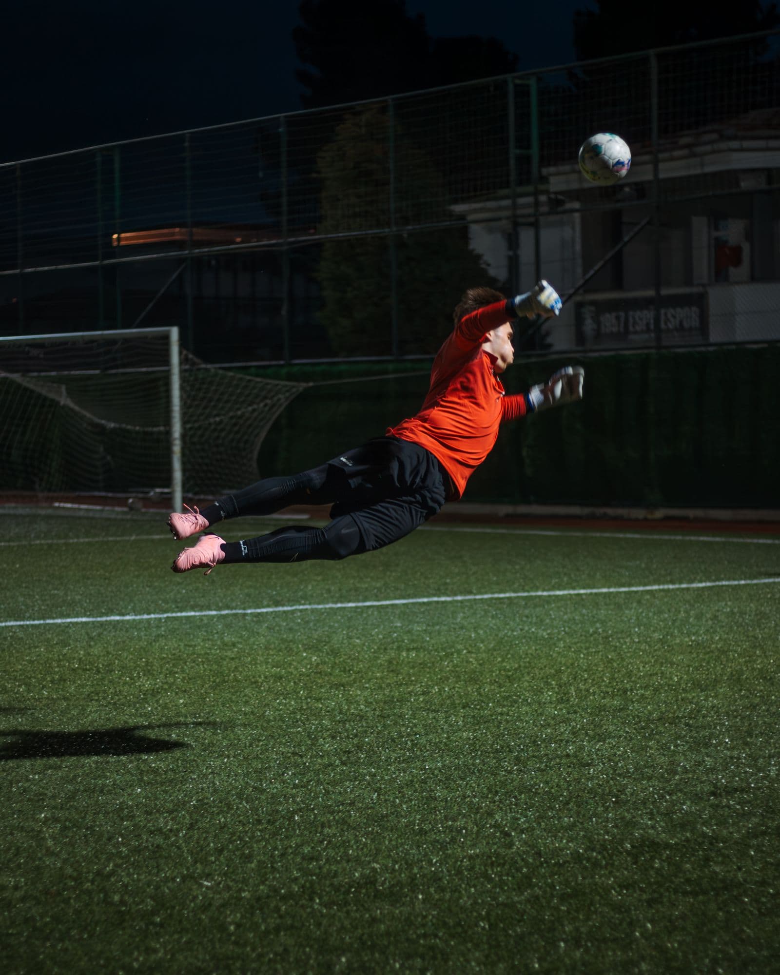 A goalkeeper diving at full stretch during a night training session